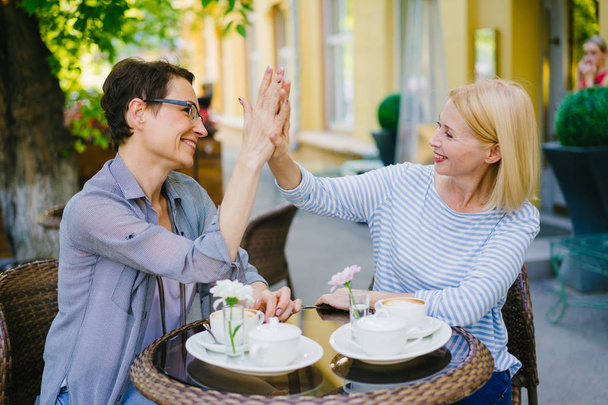 Happy women friends doing high-five and laughing in outdoor cafe in summer - Fotografie, Obrázek