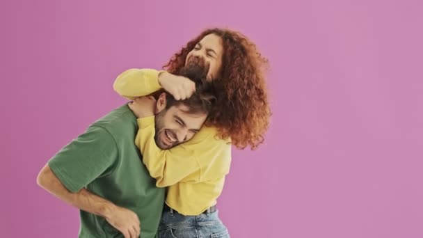 Beautiful happy young couple having fun and playing with hair while hugging over pink background isolated - Кадри, відео