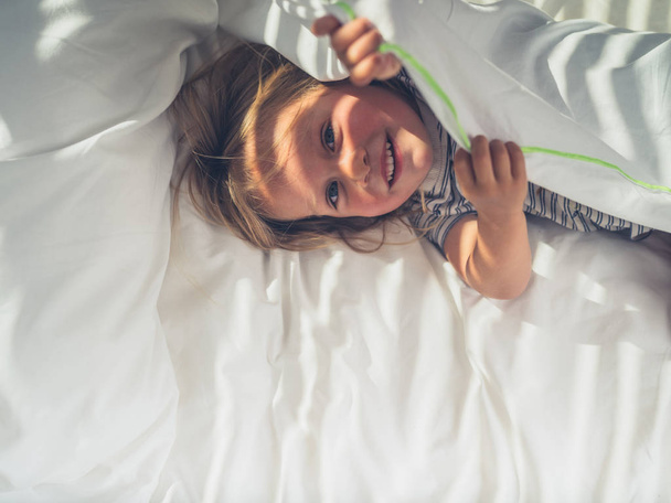 A little toddler is hiding under the covers in a bed - Foto, Bild