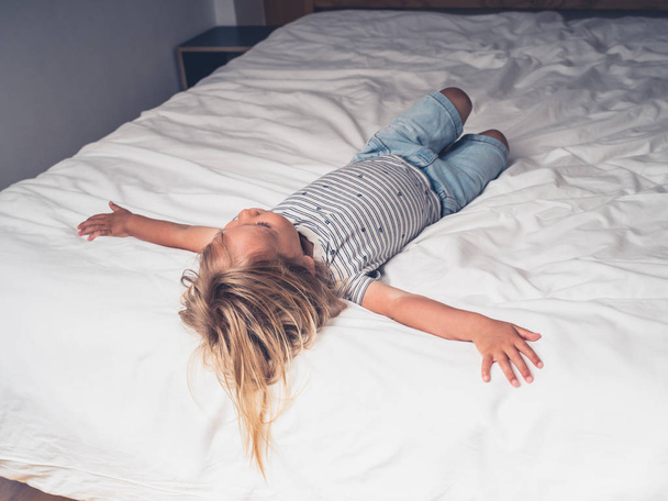 A little toddler is relaxing on the bed in a city apartment - Foto, immagini