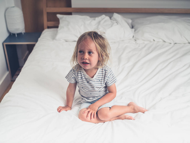 A little toddler is sitting on a bed with white sheets - Fotoğraf, Görsel