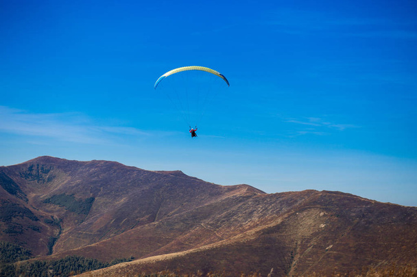 Karpat tepelerinde uçan yamaç paraşütlü siluet mavi gökyüzü arka plan üzerinde dağlar. Özgürlük hissi - Fotoğraf, Görsel