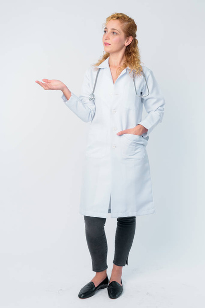 何かを示す美しいブロンドの女性医師のフルボディショット - 写真・画像