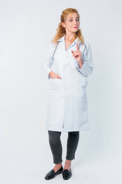Full body shot of beautiful blonde woman doctor talking while pointing finger - Foto, afbeelding
