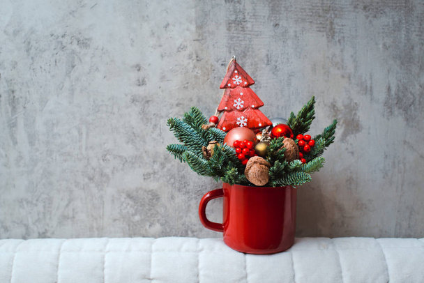 bouquet of fir branches in a red Cup and Christmas toys on a concrete background. - Фото, зображення