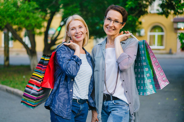 Portrait of beautiful mature ladies holding shopping bags smiling outdoors - Foto, afbeelding