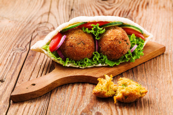 Falafel and fresh vegetables in pita bread on wooden table - Фото, изображение