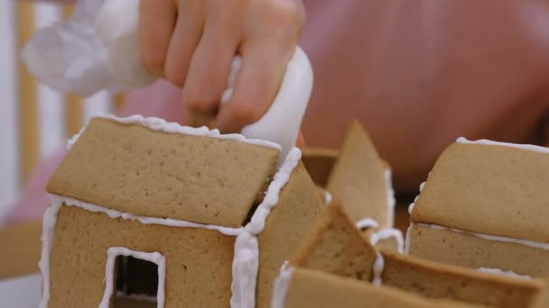 Womans hands make gingerbread houses glues details with sugar sweet icing. Cooking homemade gingerbread house. - Πλάνα, βίντεο