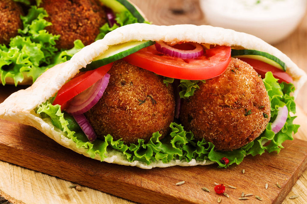 Falafel and fresh vegetables in pita bread on wooden table - Photo, image