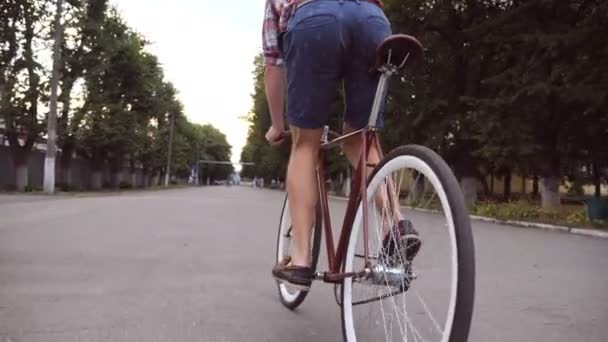 Egy fiatalember biciklizik a park útjánál. Sportos srác kerékpározik a szabadban. Egészséges, aktív életmód. Alacsony látószög Bezárás Lassú mozgás - Felvétel, videó