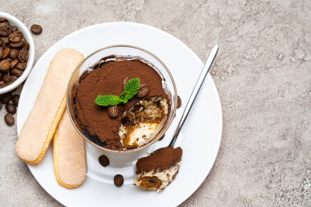 Portion of Classic tiramisu dessert in a glass, savoiardi cookies and cup of coffee on concrete background - Foto, immagini