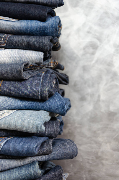Een stapel achteloos gevouwen jeans op grijze achtergrond. Close-up van jeans in verschillende kleuren. Jeans textuur of denim achtergrond. Ruimte kopiëren - Foto, afbeelding