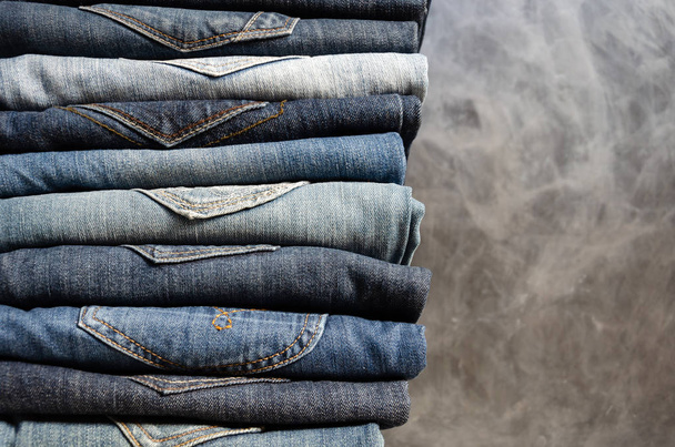A stack of neatly folded jeans on gray background. Close-up of jeans in different colors. Jeans texture or denim background. Copy space - Photo, Image