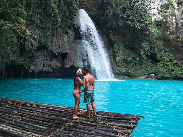セブ島の川山の滝のターコイズブルーの水で滝の前の竹いかだに一人で旅行カップル, フィリピン - 写真・画像