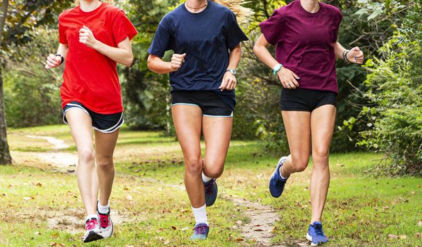Drie middelbare schoolmeisjes die samen rennen op een pad in het bos - Foto, afbeelding