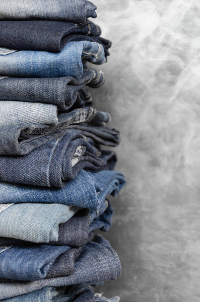 Una pila de vaqueros descuidadamente doblados sobre fondo gris. Primer plano de jeans en diferentes colores. Textura de vaqueros o fondo denim. Copiar espacio
 - Foto, imagen
