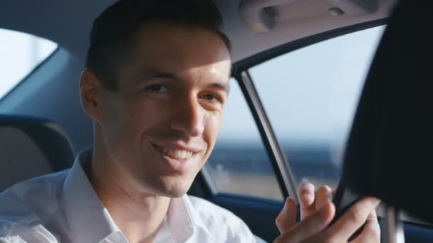 Close-Up portréja üzletember utazás autóban egy vezető. Mosolygó fiatalember fehér ing túrák a taxi - Felvétel, videó