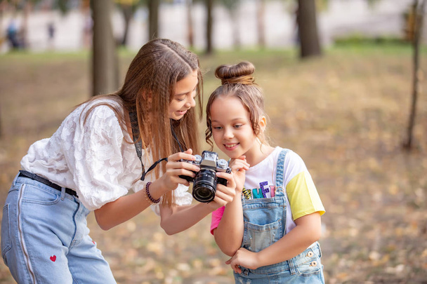 Two girls on the street make a video for the Internet, record a video blog for the camera. Children with photo appart in a city park - Fotó, kép