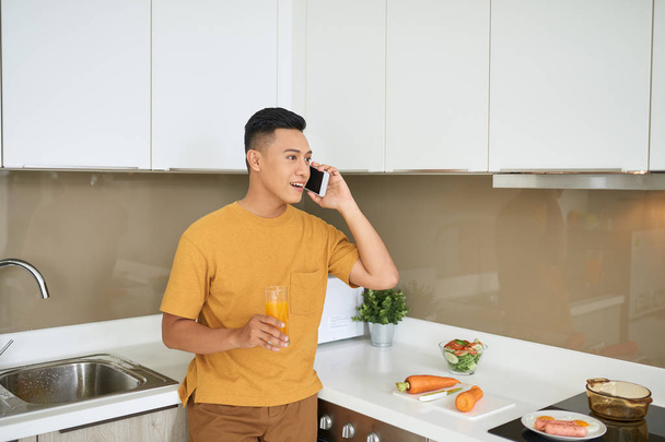 Knappe Bachelor 30s praten op mobiele telefoon, terwijl het ontbijt in de ochtend - Foto, afbeelding