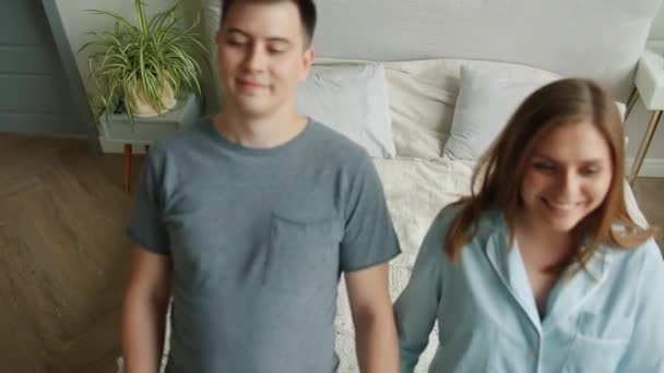Happy couple girl and guy falling on bed holding hands lying smiling relaxing - Séquence, vidéo
