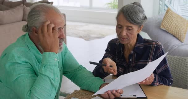 Front view close up of a mature mixed race couple holding documents and talking at home - Séquence, vidéo
