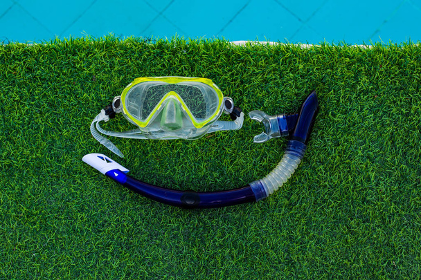Wasser Aktivität Lebensstil Objekt Bild Schnorchelbrille und Schlauch auf grünem Gras und Schwimmbad blaues Wasser Hintergrund Poster leer Kopierraum für Text  - Foto, Bild