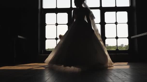 The bride in a wedding dress is spinning at the large window. Light enters the room through the window. In the hand of the bride a bouquet. - Footage, Video
