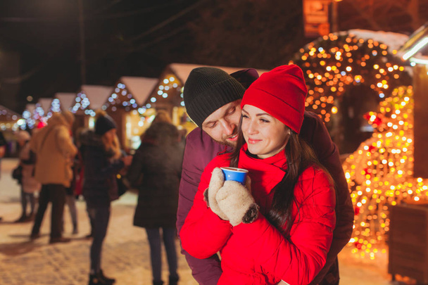 Embracing couple standing at Christams fair with a lot of lights - Foto, Imagen