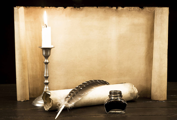 A lit candle and quill with inkwell against a background of a sc - Foto, Imagen