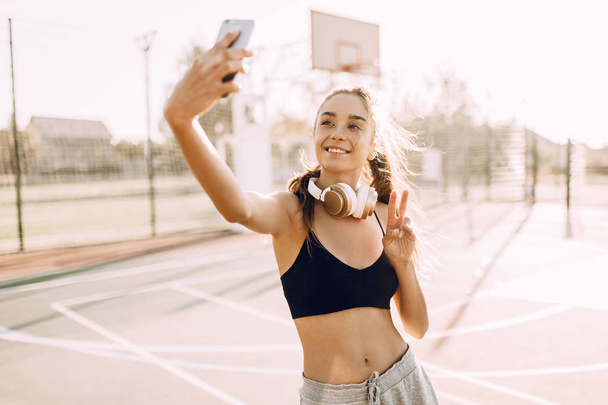 Happy fitness girl with headphones taking selfie outdoors while doing sports - Foto, imagen