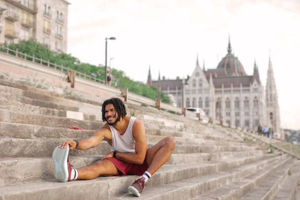A muscled man is doing stretching on the stairs after training - Foto, Imagen