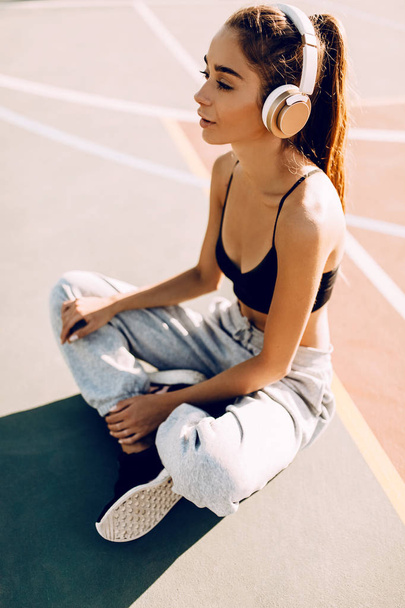 Attractive athletic young woman posing outdoors while listening to music with headphones. After a workout - Fotó, kép