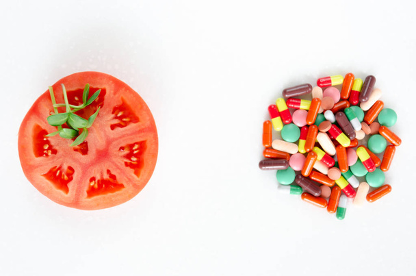 Свежие овощи против таблеток. Кусок помидоров и свежие ростки подсолнечника на куче разноцветных таблеток на белом фоне. Концепция здорового питания. Копирование пространства
 - Фото, изображение