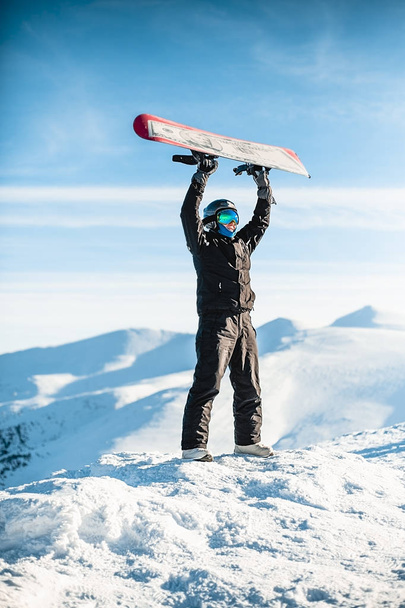 Mann hält sich in den Bergen ein Snowboard über den Kopf - Foto, Bild