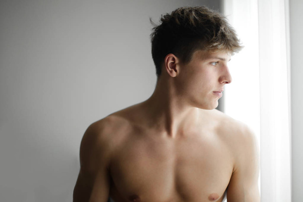 Muscled boy is looking outside the window - Photo, image