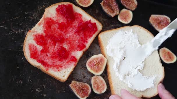 A woman spreads cream cheese and places fresh fig halves on white bread - Footage, Video