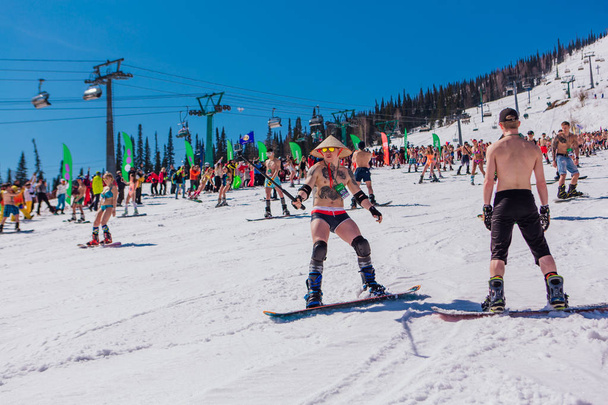 Sheregesh, Kemerovo region, Russia - April 13, 2019 : Crowd of people in bikini and shorts riding snowboard and mountain ski on the slope - Zdjęcie, obraz