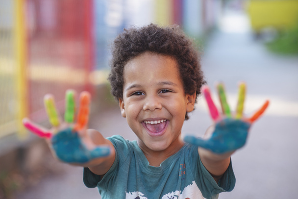 Cheerful five year old boy with hands painted in colorful paints, outdoor artistic activity concept - Photo, Image