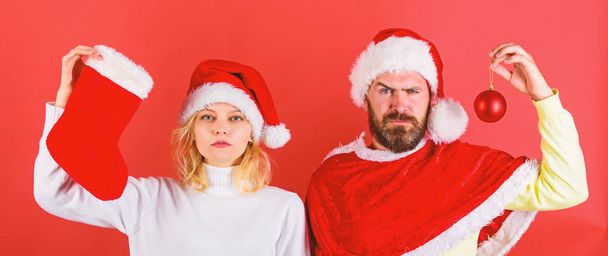 Christmas celebration concept. Woman and bearded man in santa hat waiting christmas red background. Christmas stocking tradition. Couple christmas santa costume hold sock and ornament ball - Foto, Imagen