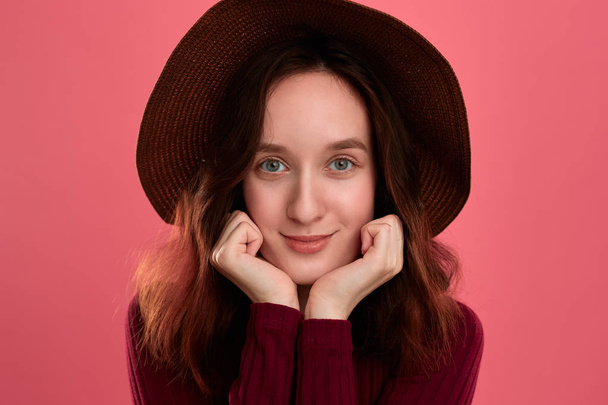 Close-up portrait of a happy beautiful brunette girl in a wide-brimmed hat posing on a dark pink background. - Photo, Image