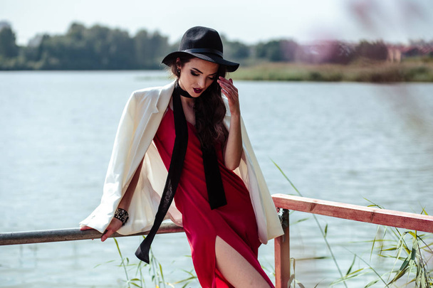 Bright portrait of brunette woman in a red dress and white jacket posing on nature. Fashion beauty photo - Фото, изображение