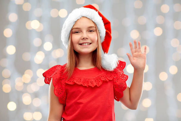 smiling girl in santa helper hat waving hand - Foto, afbeelding