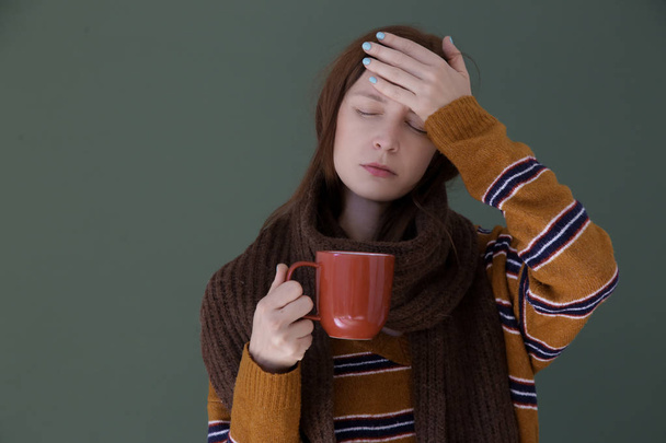 Γρίπη, κρύωμα ή αλλεργικό σύμπτωμα. Φωτογραφία στούντιο με νεαρό πυρετό γυναίκα τυλιγμένο σε ένα μαλλί κασκόλ και να έχει ένα φλιτζάνι τσάι. - Φωτογραφία, εικόνα