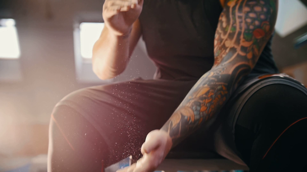 М'язистий татуйований чоловік прикриває руки в талісман і чіпляється за нього сидячи в тренажерному залі потираючи пил між пальцями
 - Кадри, відео