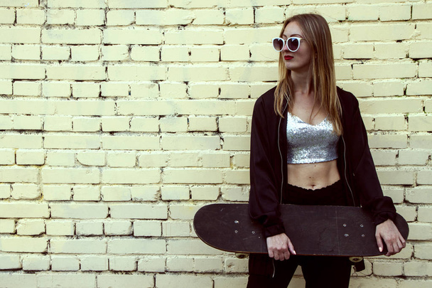 mulher da moda com um skate no fundo do tijolo. Menina em óculos de sol com longboard
 - Foto, Imagem