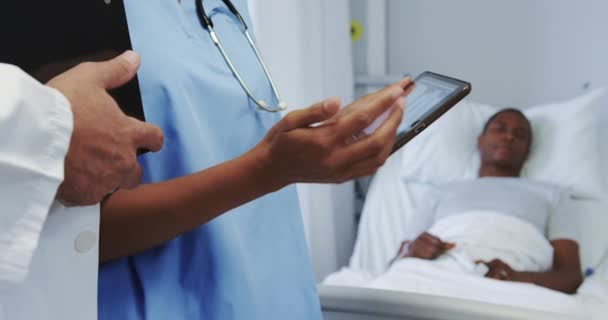 Крупный план многонациональных врачей, обсуждающих рентгеновский отчет о цифровом планшете в отделении больницы. Мужчина спит на больничной койке
  - Кадры, видео