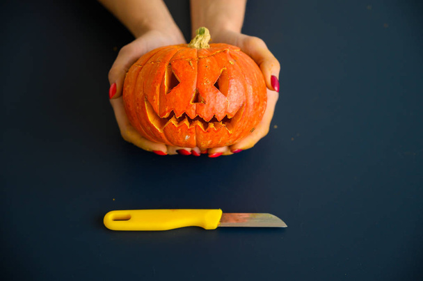  Woman holds a little pumpkin over black background. Halloween concept, flat lay, top view. knife and pumpkin in hand on a black table. - Foto, imagen
