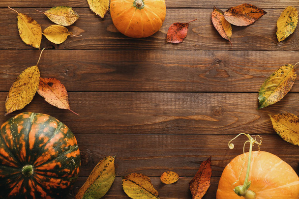 Harvest or Thanksgiving background with pumpkins and dried fall leaves on wooden table. Flat lay composition, top view, copy space - Photo, image
