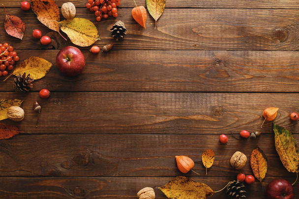 乾燥した秋の葉、リンゴ、赤い果実、木製のテーブルの上にクルミで作られた秋のフレーム。感謝祭、ハロウィーン、秋の収穫の概念。フラットレイコンポジション、トップビュー、コピースペース - 写真・画像