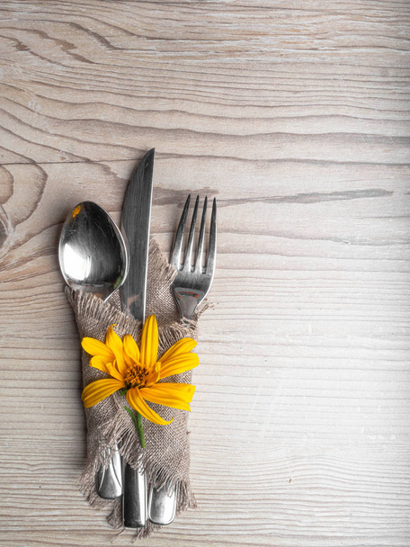 Rustic table setting with linen napkin, cutlery, yellow lower on wooden table. Holiday table decoration. Romantic dinner. - Photo, Image